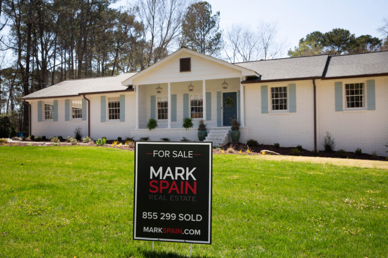 White brick home with great landscaping and for sale sign.